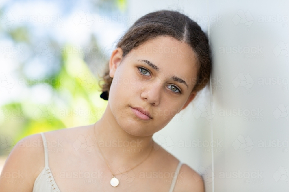 Teen girl resting her head on the white wall - Australian Stock Image