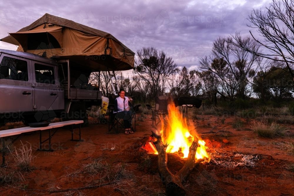 Teen girl sits by the fire at dusk in camp set up in outback Northern Territory - Australian Stock Image