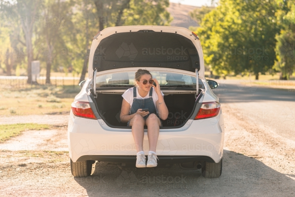 teen girl sitting in boot of car on a road trip - Australian Stock Image