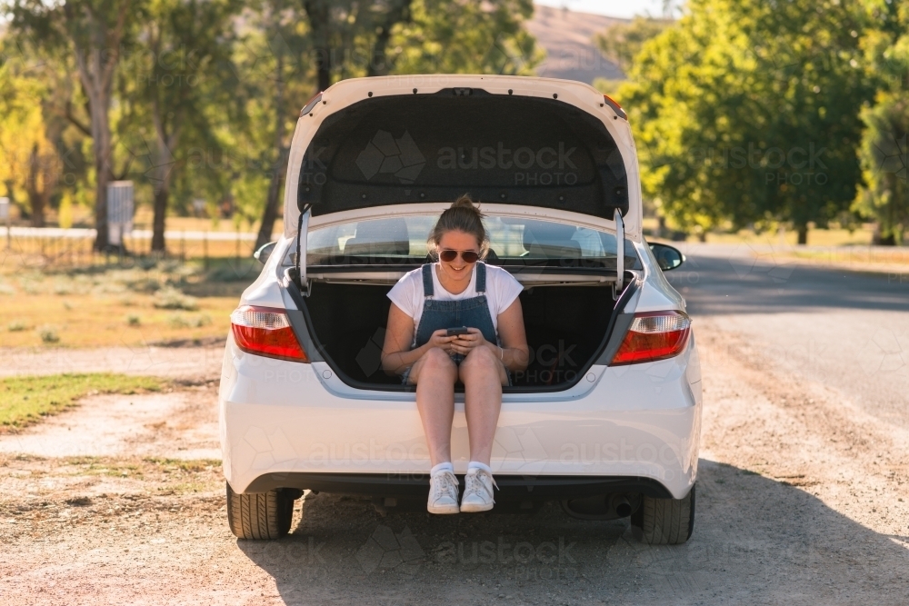 teen girl sitting in boot of car on a road trip - Australian Stock Image