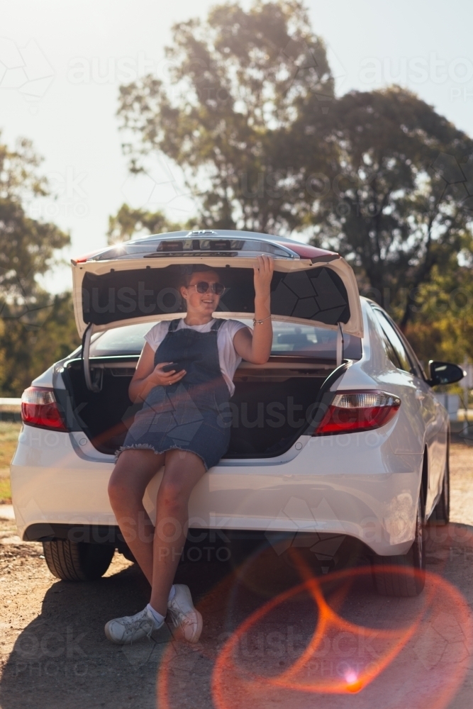 teen girl sitting in boot of car on a road trip - Australian Stock Image