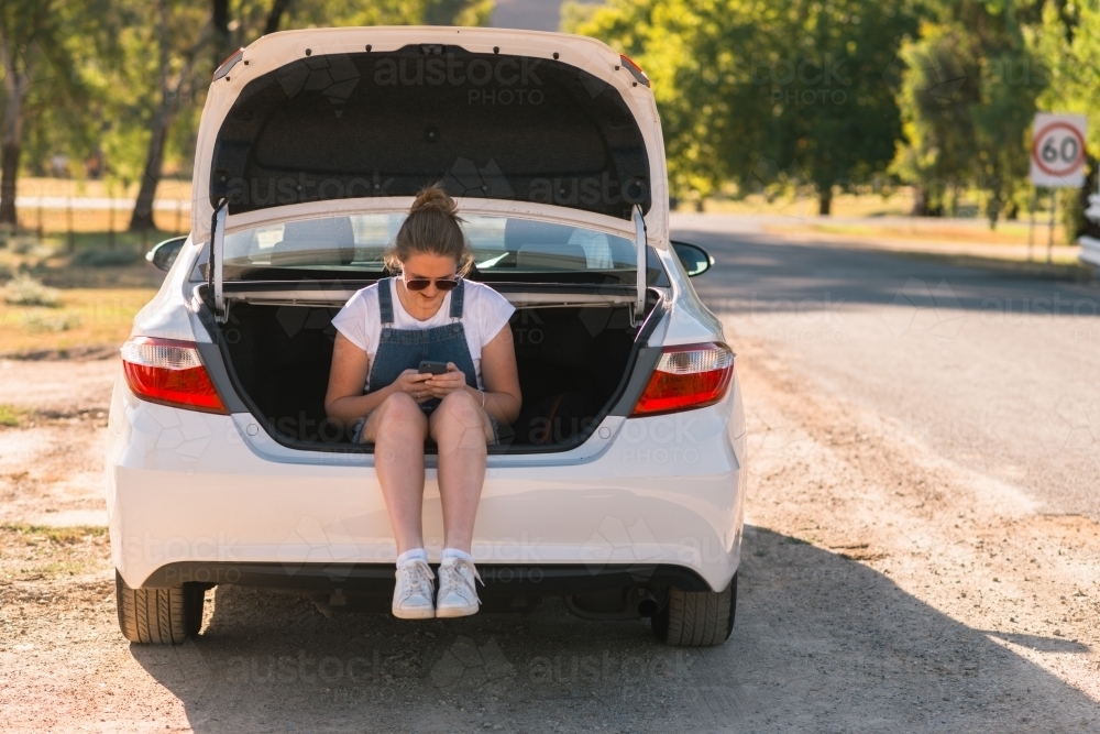 teen girl sitting in boot of car on a road trip - Australian Stock Image