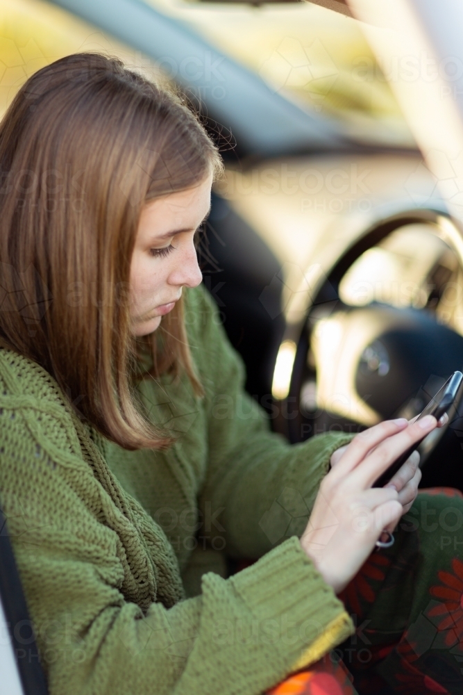 Teen girl sitting in car texting on smartphone - Australian Stock Image