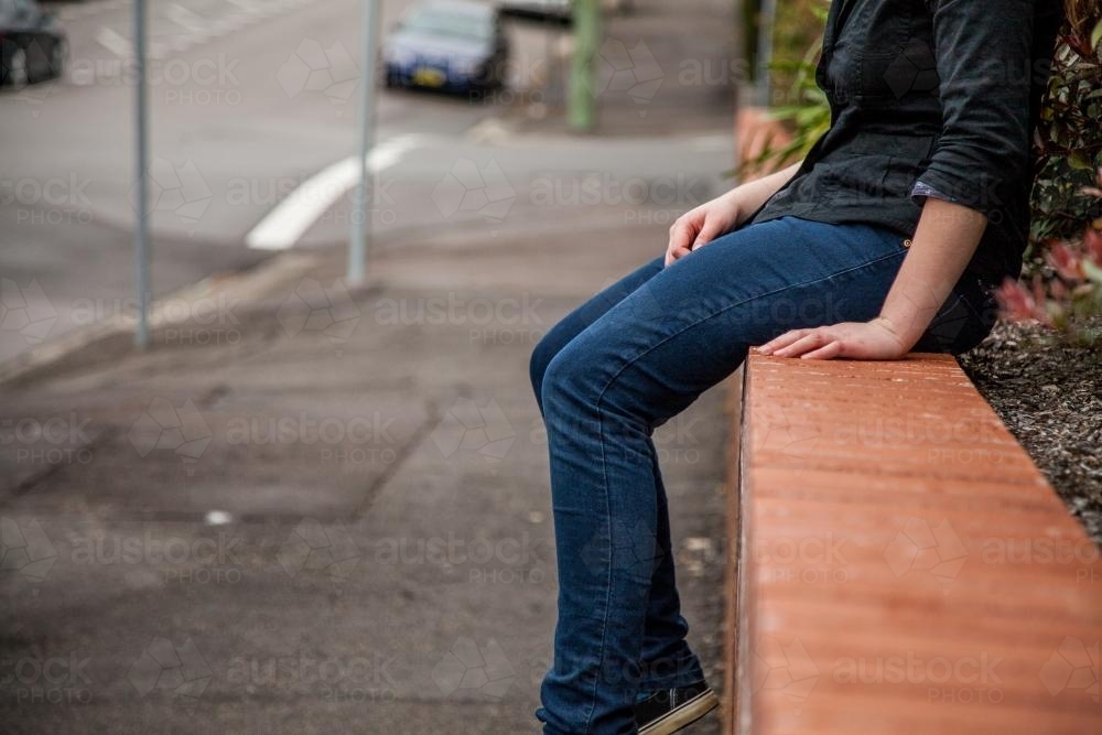 Teen girl sitting on a streetside brick wall - Australian Stock Image