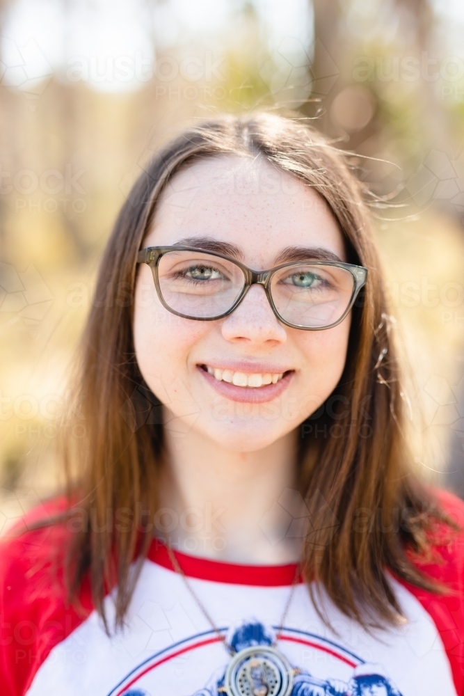 Teen girl smiling at camera wearing glasses in afternoon sun - Australian Stock Image