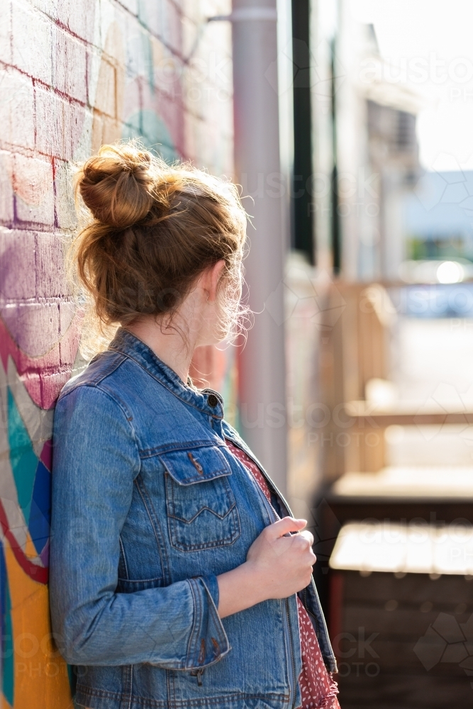 Teen girl standing in alley way leaning back against wall in urban area of country town - Australian Stock Image