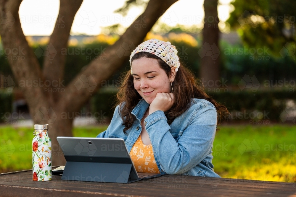 Teen girl using laptop at park working on school work - Australian Stock Image