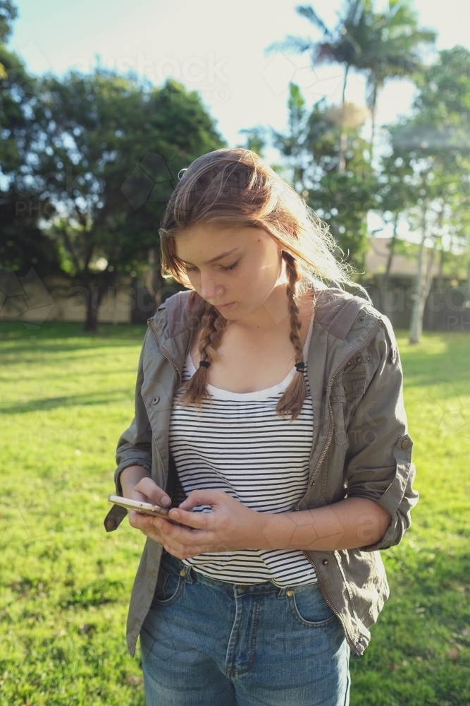 Teen girl using mobile phone while walking in the park - Australian Stock Image