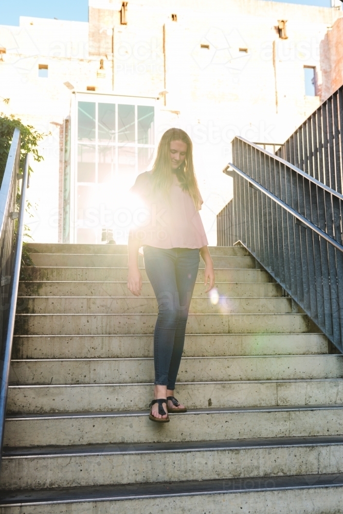 teen girl walking down stairs, backlit by a sun flare reflection - Australian Stock Image