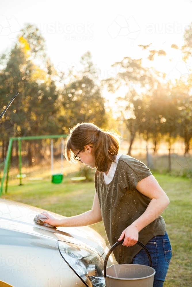 Teen girl washing family car in natural afternoon sunlight - Australian Stock Image