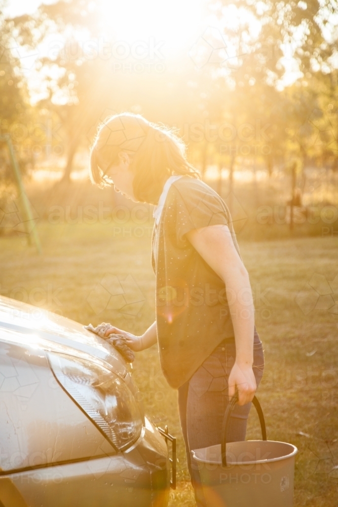 Teen girl washing family car with golden sun flare - Australian Stock Image