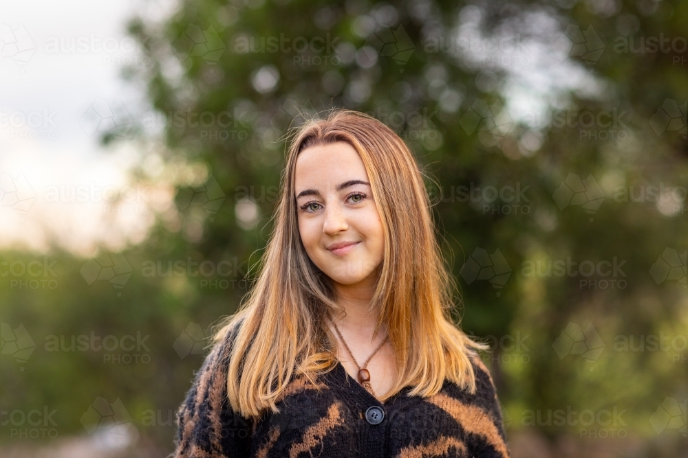 teen girl with a closed mouth smile standing outdoors - Australian Stock Image