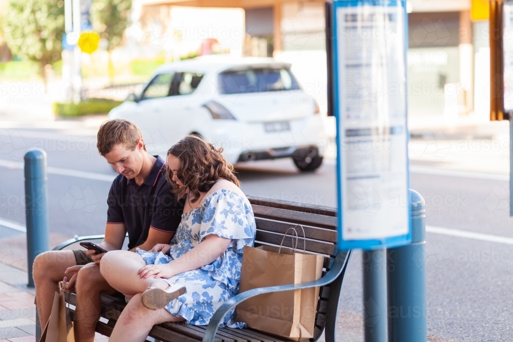 Teen girl with down syndrome at bus stop to travel on public transport checking time on phone - Australian Stock Image