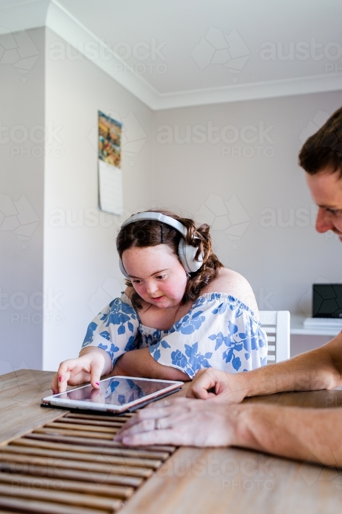 Teen girl with down syndrome listening to music on tablet with headphones - Australian Stock Image