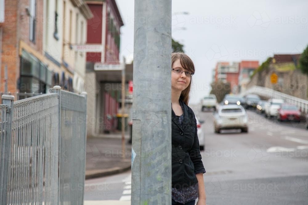 Teen girl with glasses standing beside a metal pole on the street - Australian Stock Image