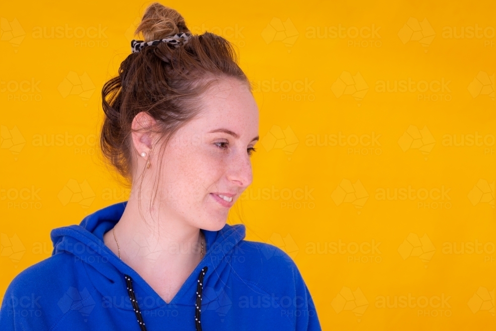 teen girl with messy bun and blue hoody against yellow background - Australian Stock Image