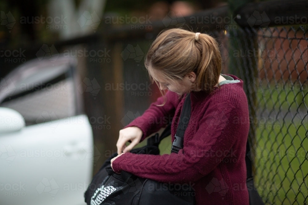 Teen girl zipping up duffel bag near car - Australian Stock Image