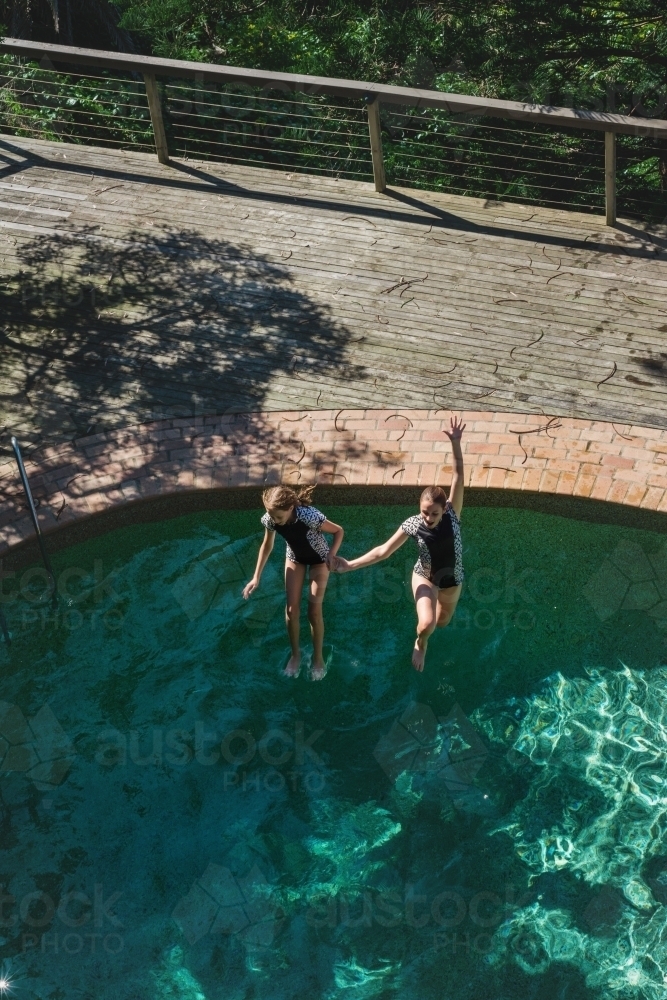 Image of teen girls jumping in a swimming pool - Austockphoto