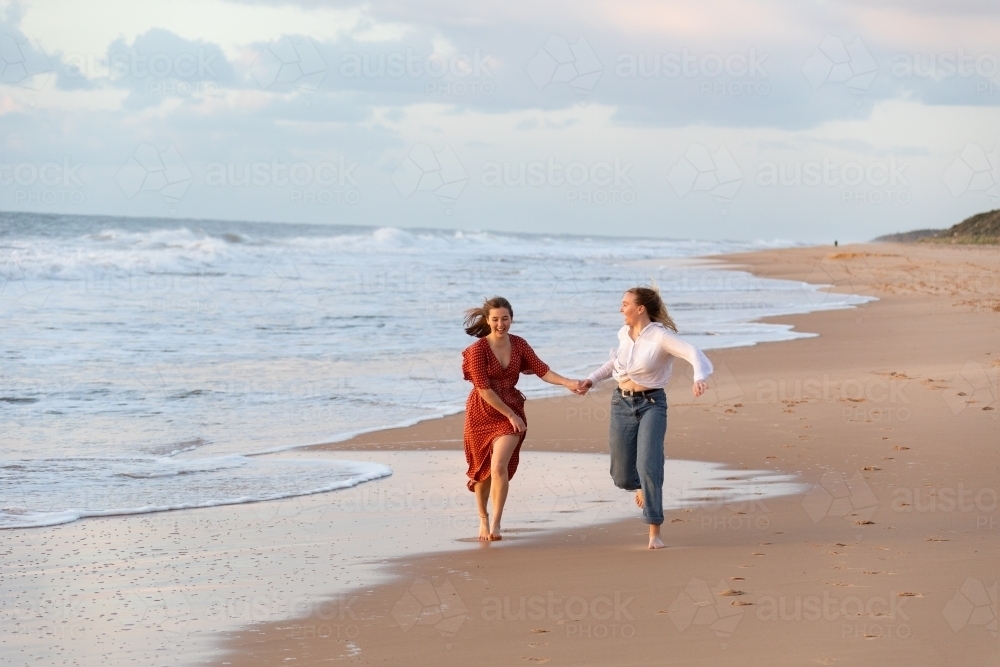 teen girls running on beach hand in hand - Australian Stock Image
