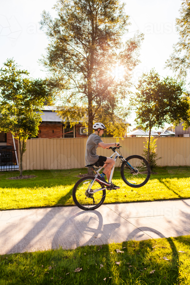 Teen kid doing wheelie on his pushbike on bike path at park - Australian Stock Image
