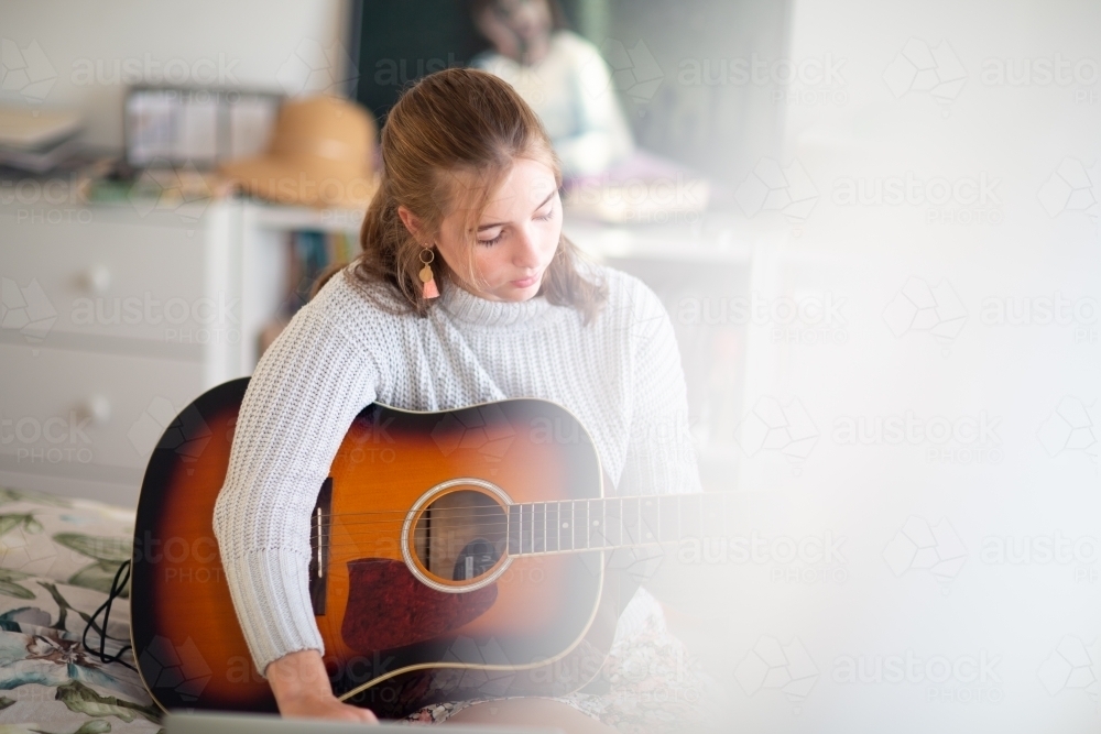 Teen learning guitar partly obscured by curtain - Australian Stock Image
