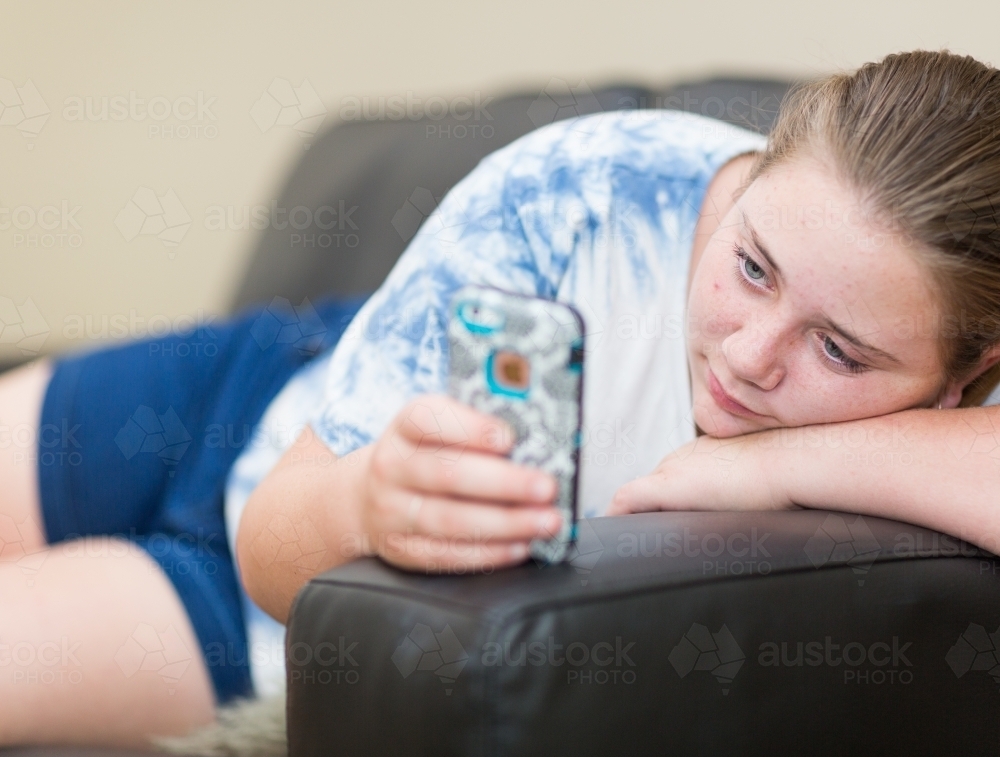 teen lounging on sofa looking at mobile phone - Australian Stock Image