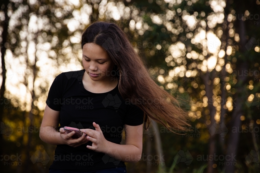 teen scrolling on phone outside - Australian Stock Image