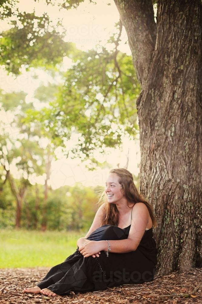 Teen sitting under a tree laughing - Australian Stock Image