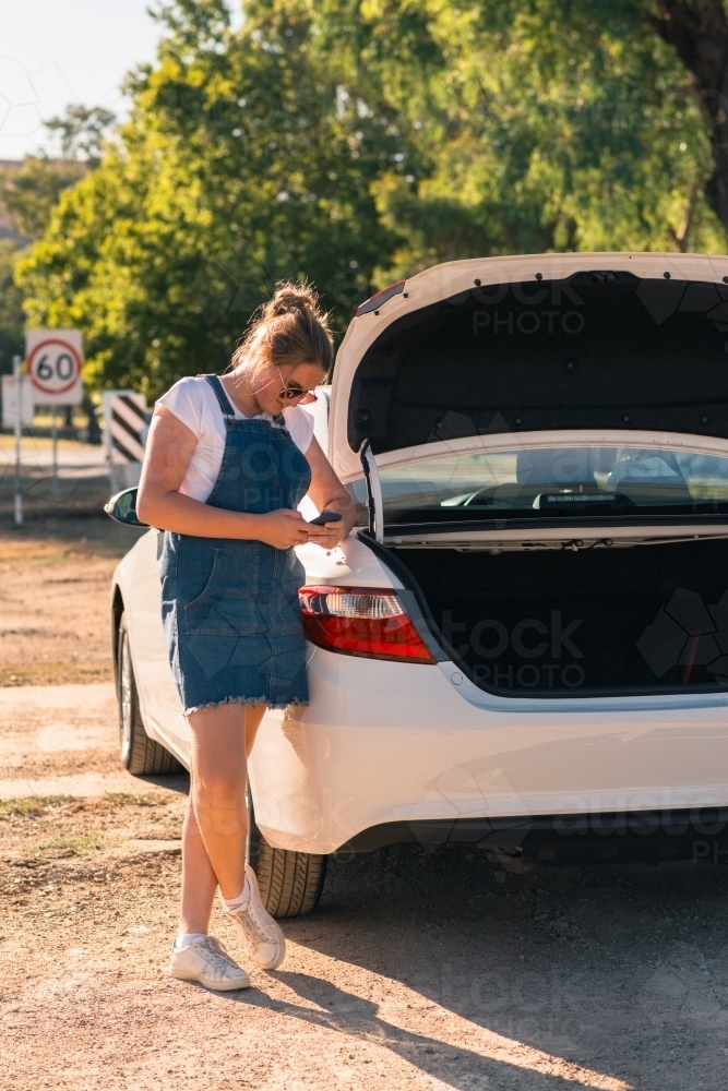 teen standing by car using mobile phone - Australian Stock Image