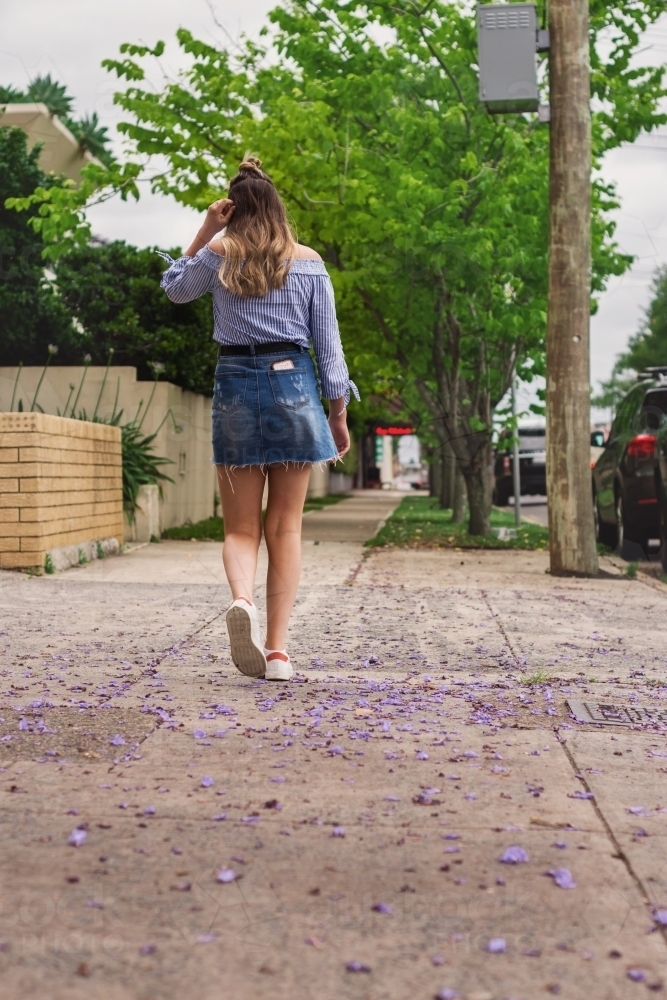 teen walking on the footpath, with jacaranda petals - Australian Stock Image