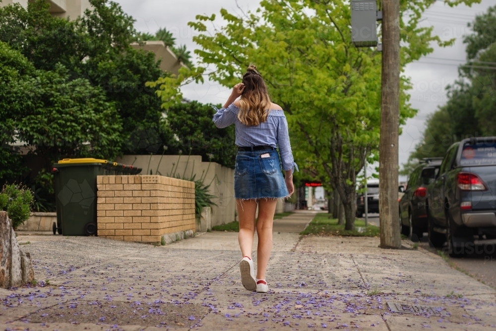 teen walking on the footpath, with jacaranda petals - Australian Stock Image