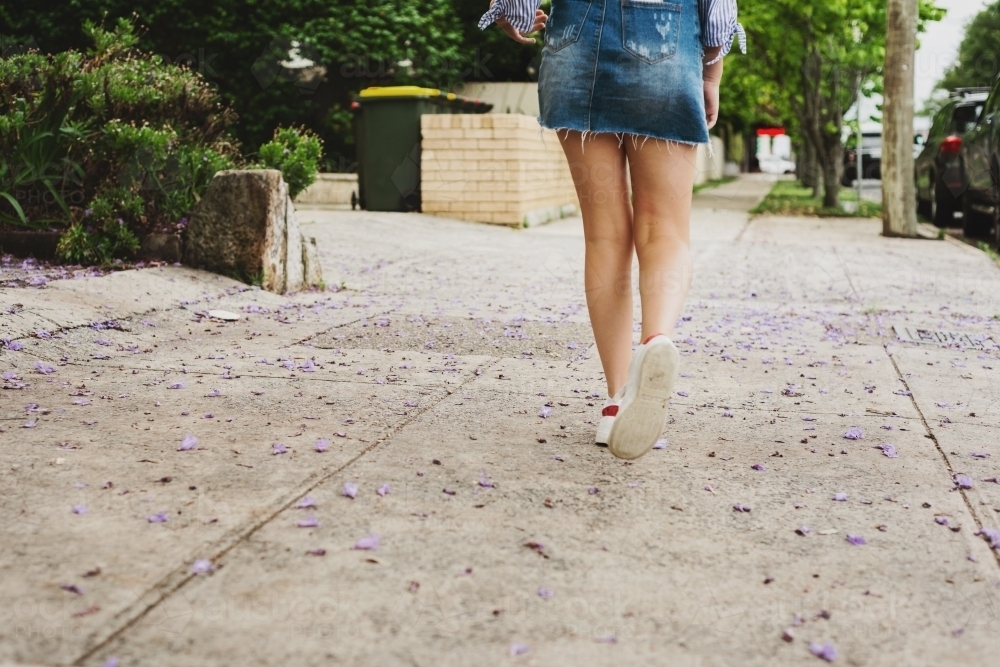 teen walking on the footpath, with jacaranda petals - Australian Stock Image