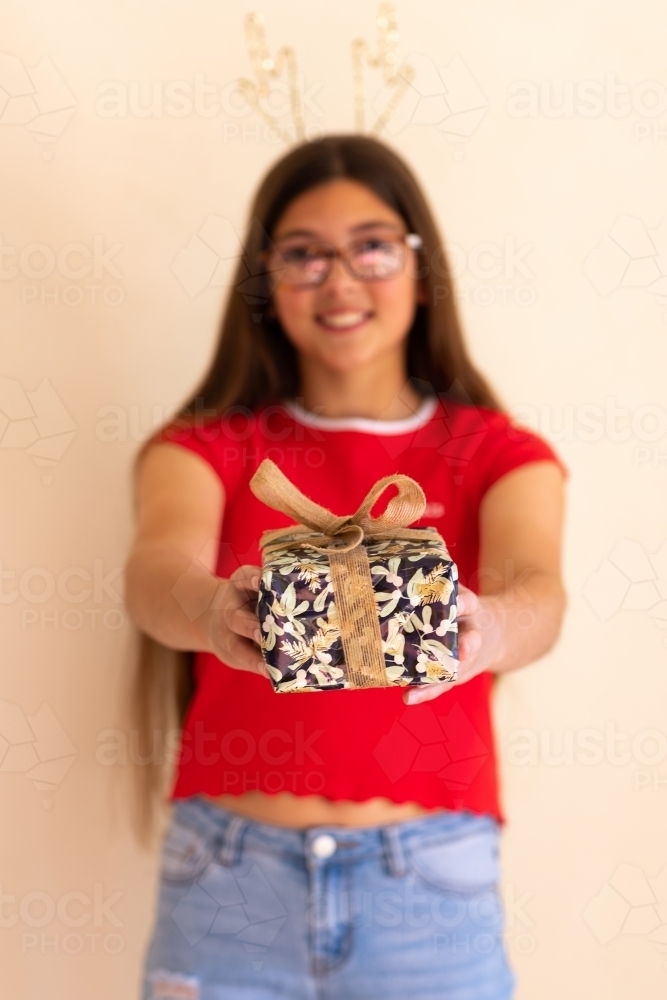 teen with long hair and glasses holding out gift-wrapped box - Australian Stock Image