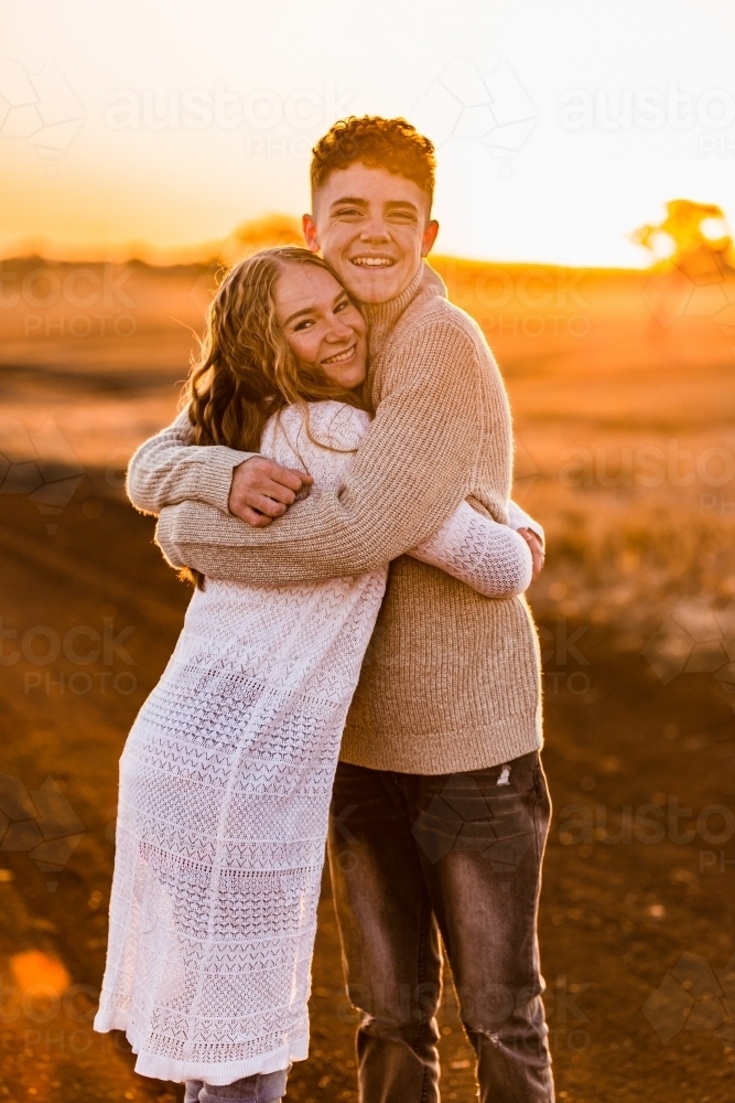 Teenage boy and girl hugging on rural dirt road at sunset - Australian Stock Image