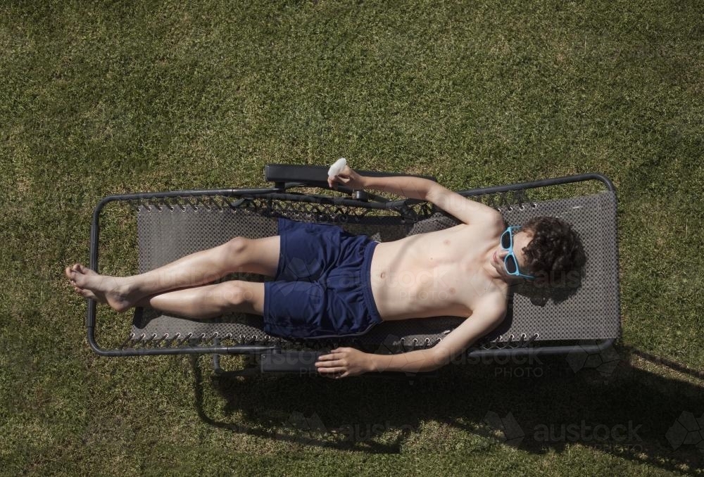 Teenage boy eating icypole while sunbaking - Australian Stock Image