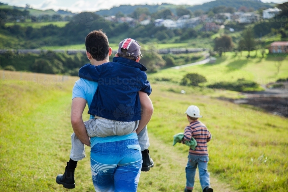 Teenage boy giving a piggyback ride to kid on a bushwalk - Australian Stock Image