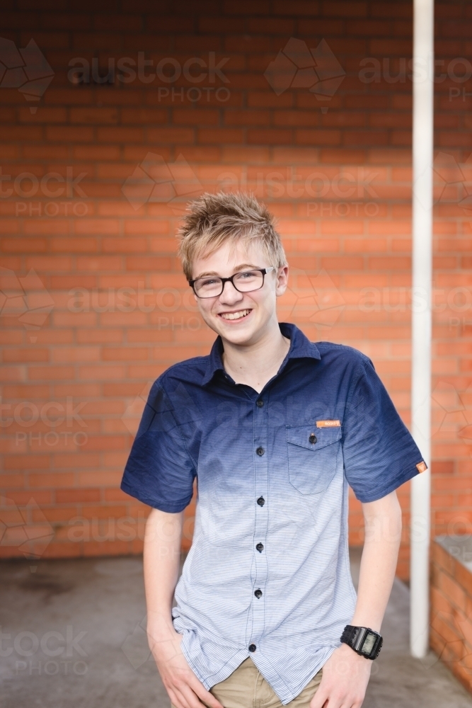 Teenage boy in front of red bricks smiling at camera - Australian Stock Image