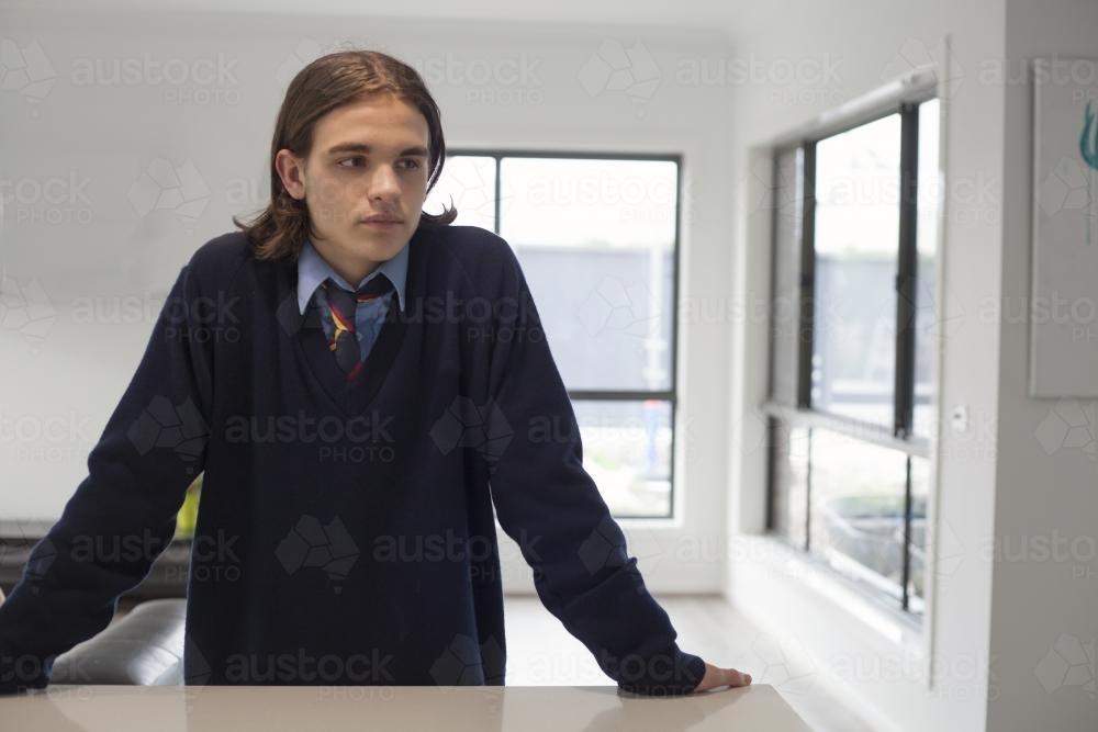 Teenage boy in high school uniform leaning on a bench at home - Australian Stock Image
