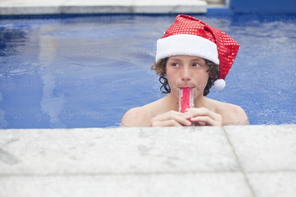 Teenage boy in Santa hat celebrating christmas in a pool - Australian Stock Image