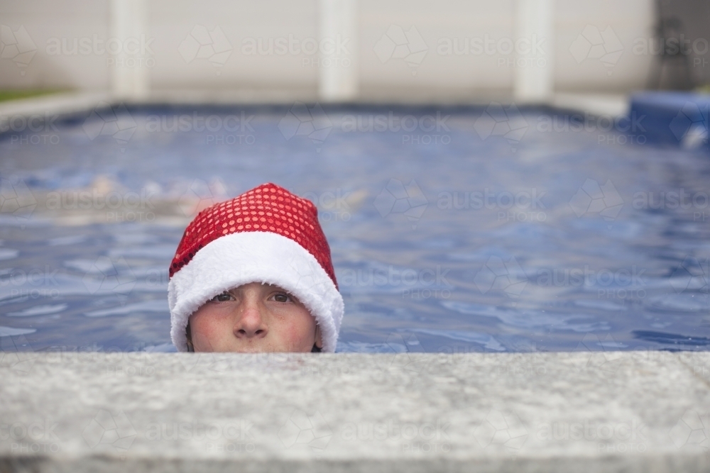 Teenage boy in Santa hat celebrating christmas in a pool - Australian Stock Image