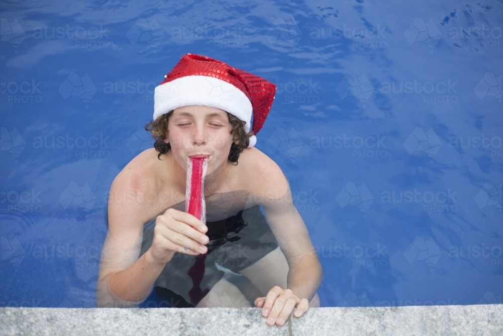 Teenage boy in Santa hat celebrating christmas in a pool - Australian Stock Image