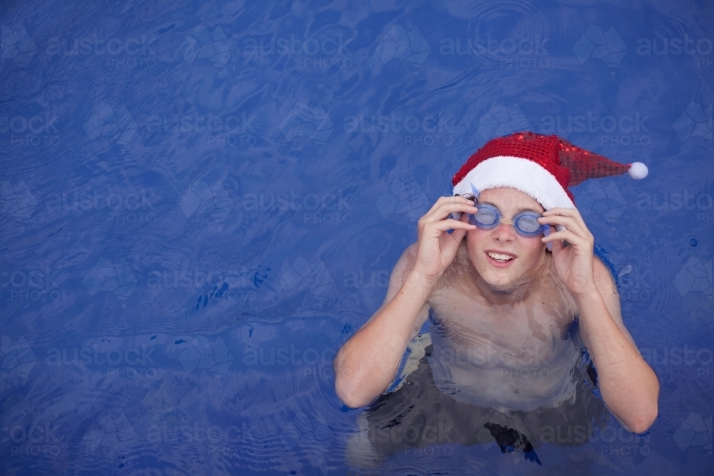 Teenage boy in Santa hat celebrating christmas in a pool - Australian Stock Image