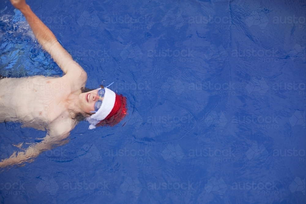 Teenage boy in Santa hat celebrating christmas in a pool - Australian Stock Image
