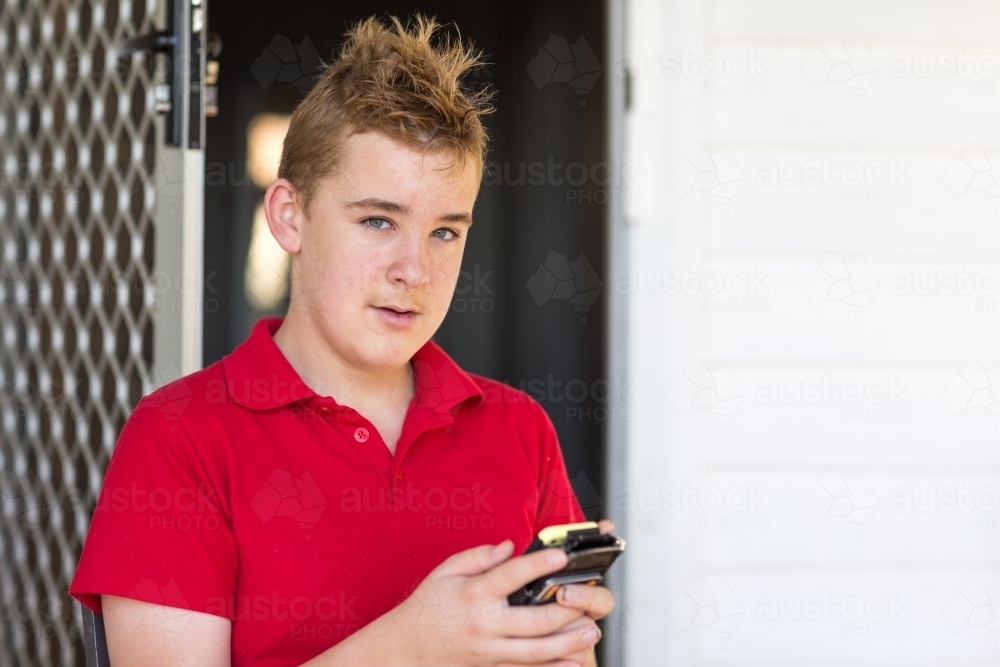 Teenage boy looking at camera while texting on phone - Australian Stock Image