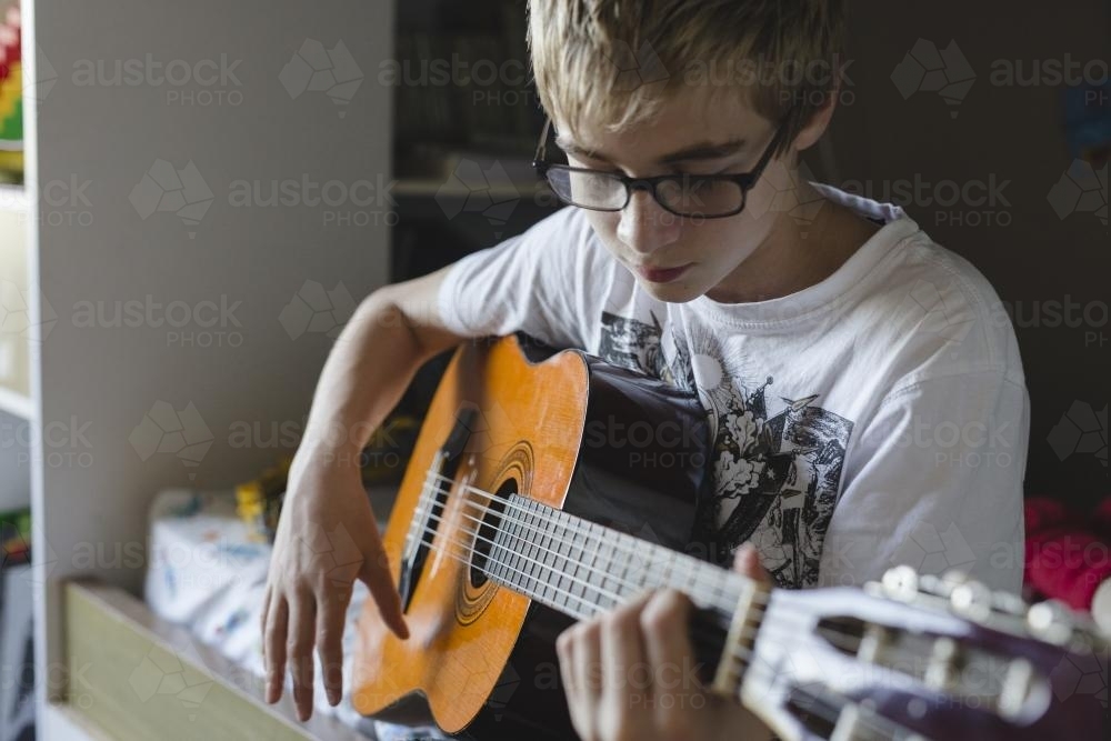 Teenage boy playing guitar in his bedroom - Australian Stock Image