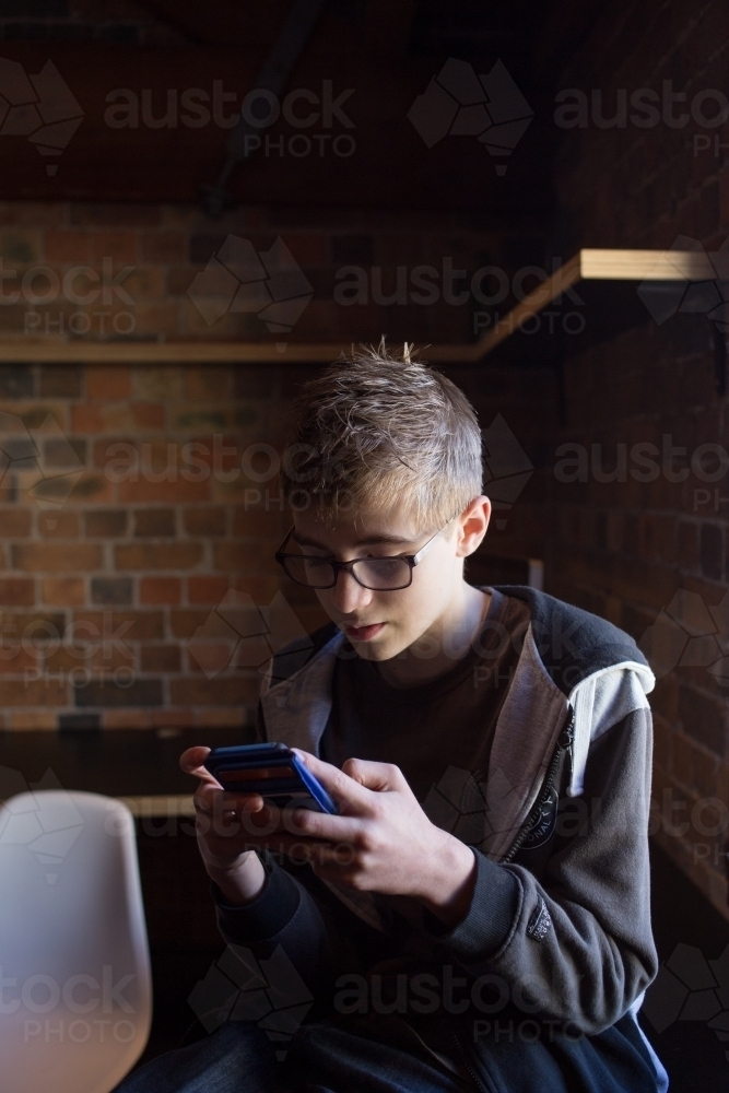 Teenage boy playing on mobile device - Australian Stock Image