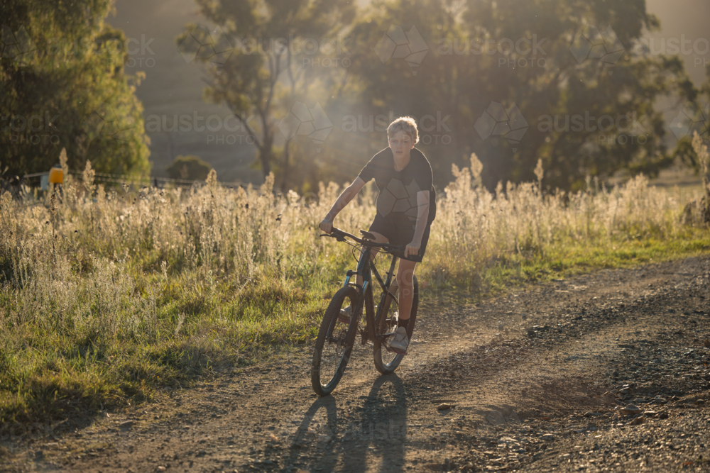 Teenage boy riding mountain bike in rural countryside bathed in golden afternoon light - Australian Stock Image