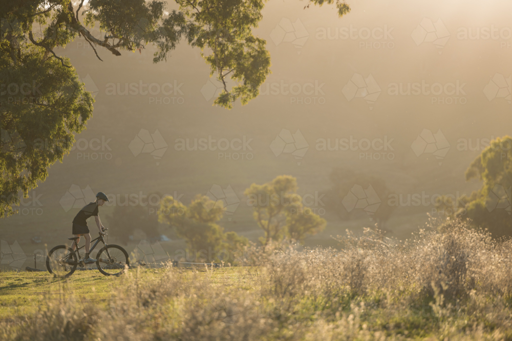 Teenage boy riding mountain bike in rural countryside bathed in golden afternoon light - Australian Stock Image