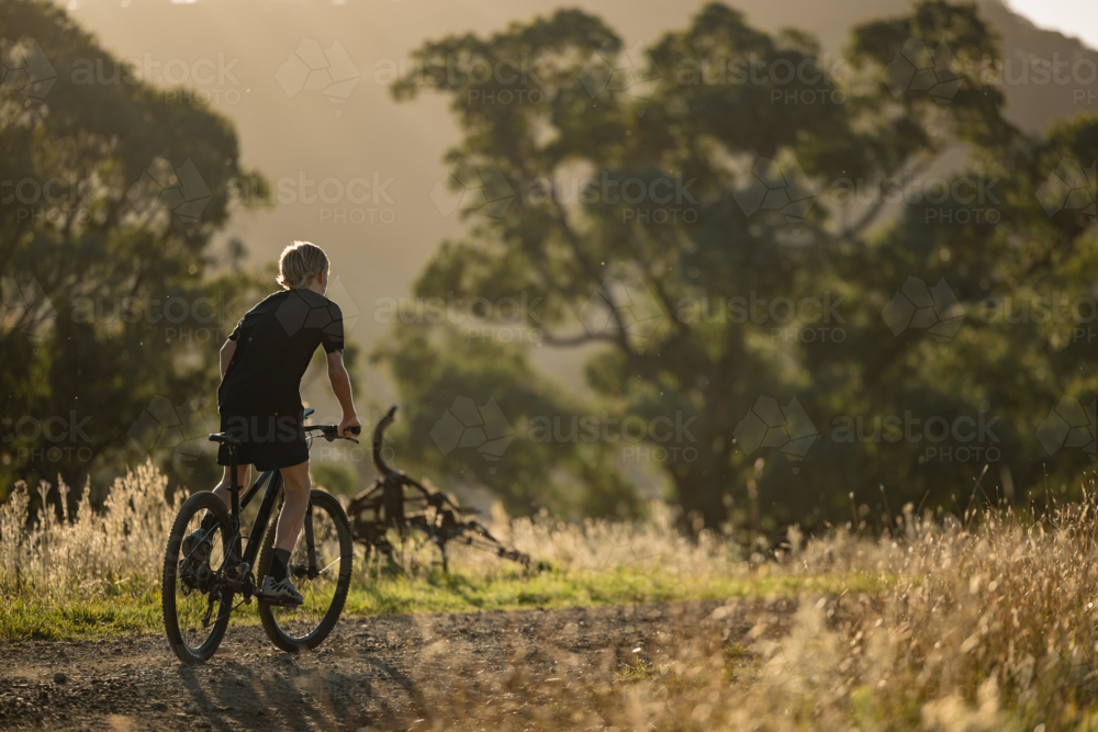 Teenage boy riding mountain bike in rural countryside bathed in golden afternoon light - Australian Stock Image