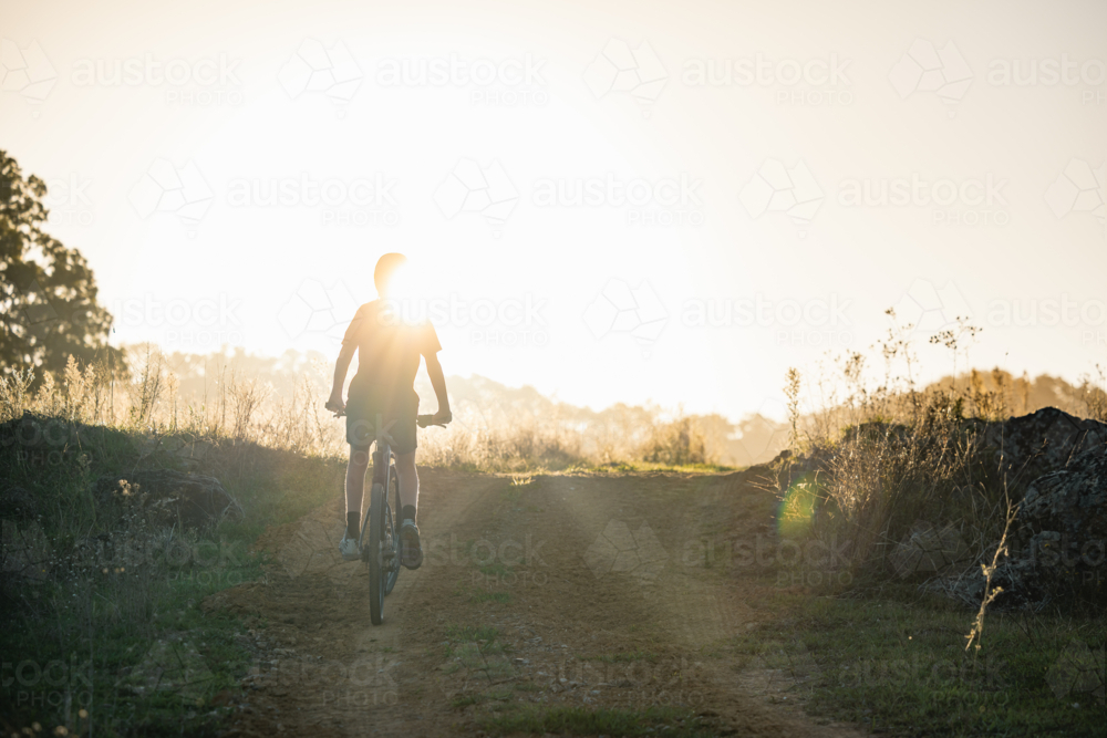 Teenage boy riding mountain bike in rural countryside bathed in golden afternoon light - Australian Stock Image
